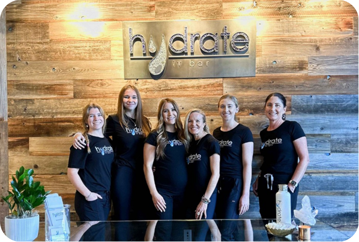 The Hydrate IV Bar team in front of the branded reclaimed-wood feature wall